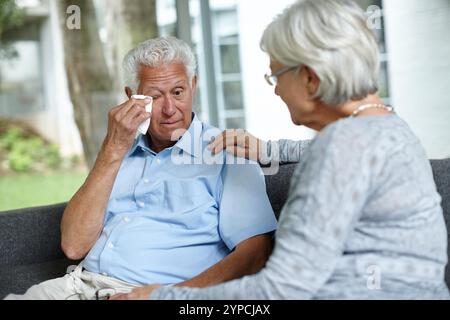 Home, senior couple and crying with comforting husband on couch in living room for love and support. People, relationship and sad with consoling for Stock Photo