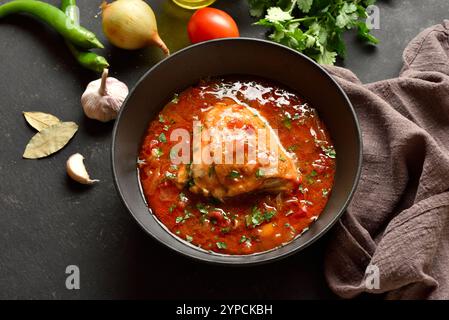 Baked chicken with tomato gravy and herbs in bowl over dark stone background. Tasty homemade chicken stew for dinner. Close up view Stock Photo