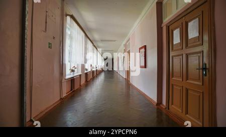 Deserted school hallway with pink walls, wooden doors, and windows adorned with curtains, evoking a sense of quietude on the last day of school Stock Photo