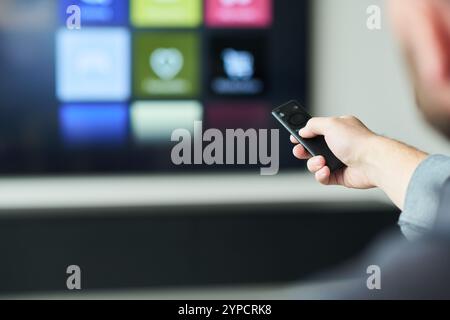 Close-up of hand holding remote control while interacting with smart TV screen displaying multiple app icons. Person navigating through settings and media options in relaxed setting Stock Photo