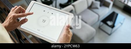 Adjusting temperature settings on smart tablet used for home temperature control in modern living room with white walls and minimal design Stock Photo
