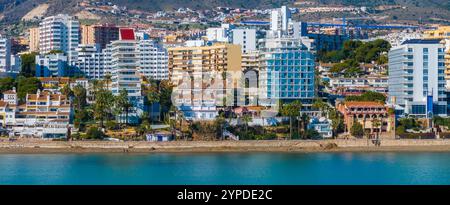 Benalmadena, Spain features a sandy beach with turquoise sea, modern high rises, traditional architecture, palm trees, and rolling hills in the backgr Stock Photo