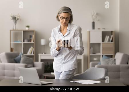 Focused middle aged entrepreneur woman using mobile phone at home Stock Photo