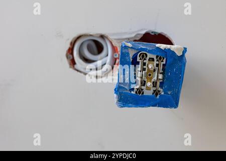 Close-up view of an electrical outlet installation in progress with protective blue tape and exposed wires in a drywall panel Stock Photo