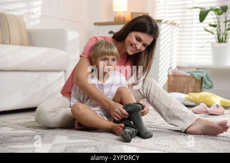 Mother helping her daughter to put tights on at home Stock Photo