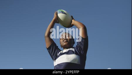 Front view low angle of a young adult biracial female rugby player shouting and throwing the ball to Stock Photo