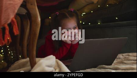 Caucasian girl smiling while using laptop under blanket fort during christmas at home Stock Photo