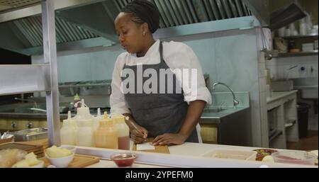 Front view of an African American female cook working in a busy restaurant kitchen, checking and wri Stock Photo