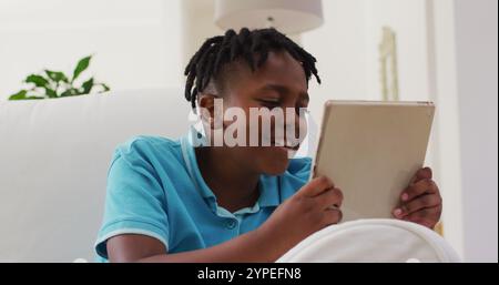 African american boy smiling while using digital tablet sitting on the couch at home Stock Photo