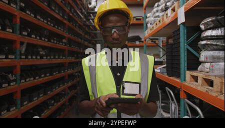 An African American male worker at a factory, using a tablet computer, walking in a warehouse storag Stock Photo