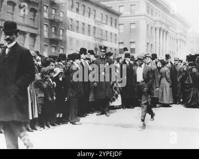 Police officers maintain order among mourners lined up outside the 26th Street pier morgue, waiting to identify victims of the Triangle fire. The Triangle Shirtwaist Factory Fire was one of the worst industrial accidents in US History. A fire broke out on the 10th floor of the Asch Building. The fire exits were locked, the fire escape inadequate and the fire engine ladders were not long enough. 146 people were killed, of which 62 jumped to their deaths to avoid the flames. Stock Photo