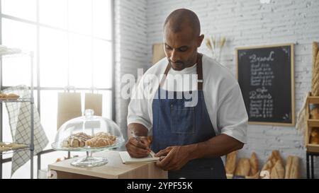 Young man working in a bakery taking notes with pastries on display and bread shelves in the background Stock Photo