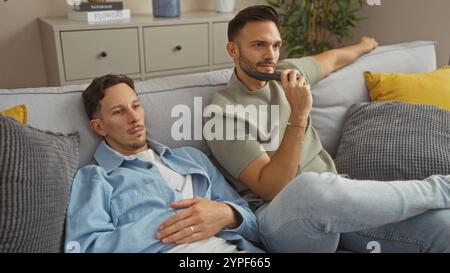 Two men relaxing in their living room, one holding a tv remote, symbolizing a cozy home environment Stock Photo