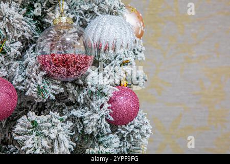 Close up of festive pink tone themed xmas baubles hanging on a christmas tree with branches covered in white snow. Copy space Stock Photo
