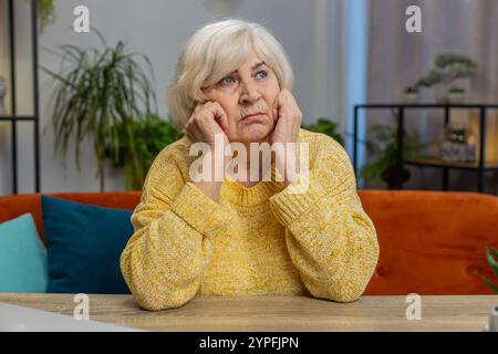 Sad stressed senior elderly old grandmother woman sits at home looks pensive thinks over life concerns suffers from unfair situation. Problem crisis depression feeling bad, sick ill, annoyed burnout Stock Photo