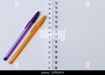 Purple and orange color pens over white paper notebook. School creative stationery. Stock Photo