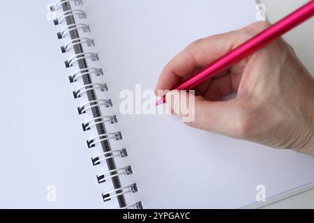 Caucasian human hand holding a pink pen to write a message on a white paper notebook. Colorful drawing, creative design and writing concept. Stock Photo