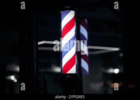 Barber pole with red, white, and blue stripes illuminated at night Stock Photo