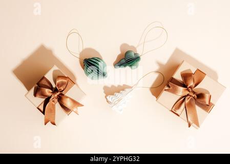 Flat lay of gift boxes with bronze ribbons, green and white paper ornaments on a beige background, top view. Stock Photo