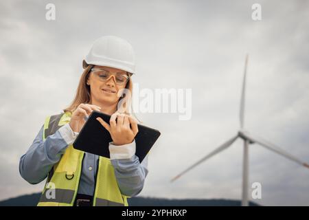 A dedicated female engineer is at a wind farm, using a tablet equipped with advanced technology to conduct thorough data analysis, showcasing Stock Photo