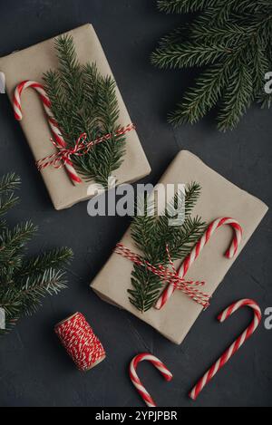 Christmas background. Gift boxes in craft paper with candy canes and coniferous tree branch on black background. Stock Photo