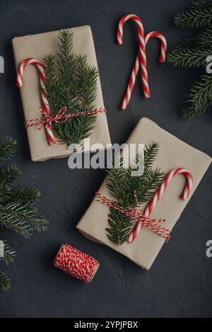 Christmas background. Gift boxes in craft paper with candy canes and coniferous tree branch on black background. Stock Photo