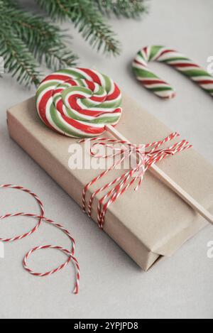 Christmas background. Gift box wrapped in craft paper with green and red lollipop and pine branch on light background. Stock Photo