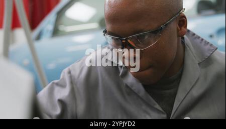African American male car mechanic working in a township workshop, holding a screwdriver, using a ha Stock Photo