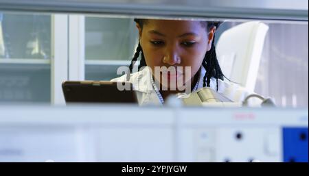 Scientist looking through microscope while using digital tablet in laboratory Stock Photo