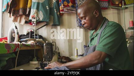 Side view of an African male tailor in a township workshop, using a sewing machine Stock Photo