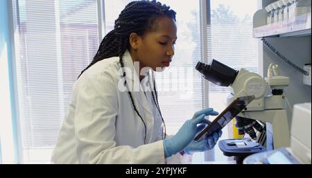 Scientist looking through microscope while using digital tablet in laboratory Stock Photo