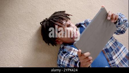 Happy african american boy using tablet lying on floor at home, slow motion Stock Photo