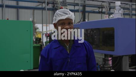 Portrait of focused African American male worker standing, looking to camera in a busy factory wareh Stock Photo