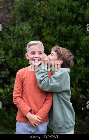 A child telling a secret to another child outdoors Stock Photo