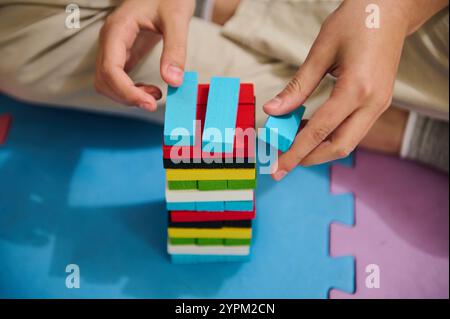 Close-up of a child stacking colorful wooden blocks on a foam play mat. The activity promotes hand-eye coordination, creativity, and cognitive skills. Stock Photo