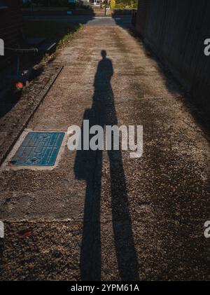 Long Shadow of a Person on Textured Pavement in a Suburban Neighborhood at Sunset Stock Photo
