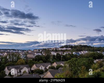 Clear skies slowly give way to clouds, signaling an approaching thunderstorm over a quiet US neighborhood on a late summer evening, creating a peacefu Stock Photo