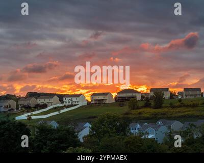 A vibrant sunset paints the sky above a suburban neighborhood, casting a warm glow over the houses and trees. Stock Photo
