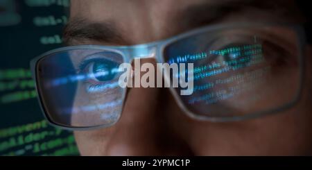 A close-up of a focused programmer's face wearing eyeglasses which reflect lines of glowing green and blue programming code. Hacker, cybersecurity and AI concept Stock Photo