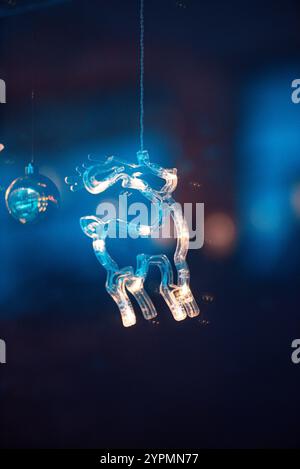 Magical Christmas scene with blue deer, bell, and tree-shaped ornaments glowing with sparkles. The colorful lights, reflected in the window Stock Photo