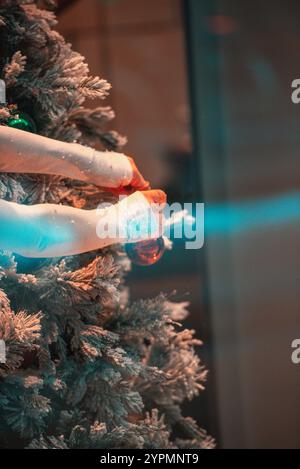 Warm orange-toned Christmas scene with festive lights and ornaments on a beautifully decorated tree. A lady’s hands are gently adding decorations Stock Photo