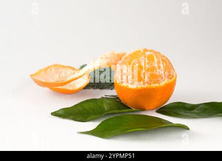 Half peeled tangerine with peel and several green leaves on light background in horizontal format Stock Photo