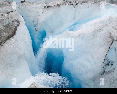 A deep ice crevasse within Mendenhall Glacier, Alaska, showcasing clear water and vibrant blue ice in the depths, emphasizing the natural glacial form Stock Photo