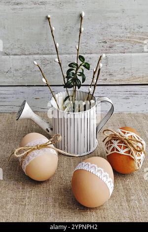 Easter scene with lace-wrapped Easter eggs, willow branches, and watering can on burlap background. Plastic-free and zero waste Stock Photo