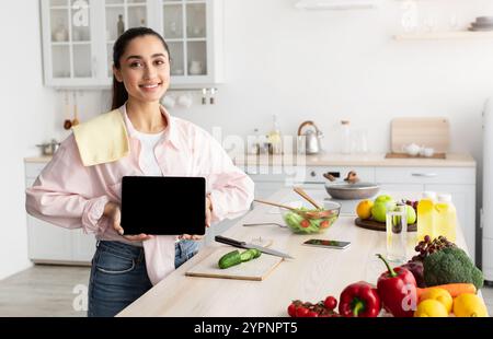 Woman showing tablet with empty screen for mockup in kitchen Stock Photo