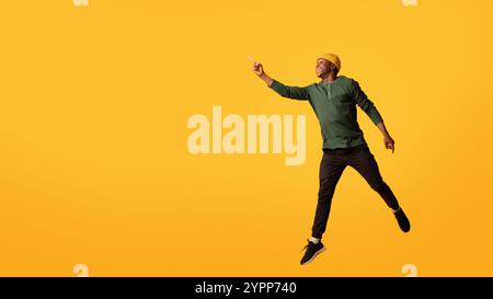 Look There. Excited African Guy Jumping And Pointing Aside At Copy Space Stock Photo