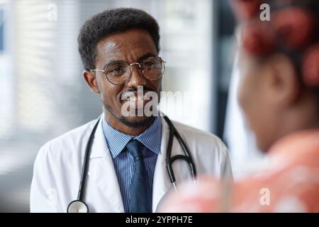 Portrait of smiling African American male doctor with stethoscope listening to female patient during consultation in clinic, copy space. Stock Photo