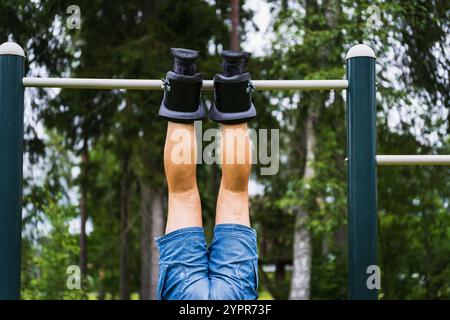A mans legs in gravity boots hangs on a horizontal bar outdoors on a summer day. Close up photo. Stock Photo