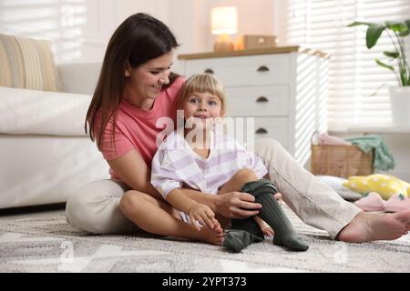 Mother helping her daughter to put tights on at home Stock Photo