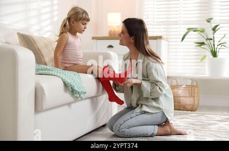 Mother helping her daughter to put tights on at home Stock Photo